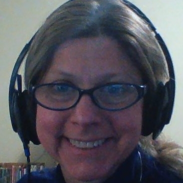 Smiling middle aged white woman wearing headset and reading glasses. Not a professional photo, but quick recent image from her pc camera to remind you that she is here to be helpful, community support volunteer.