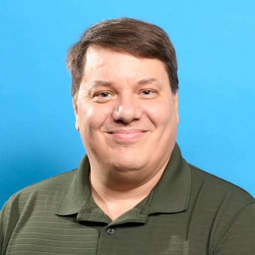 Middle-aged white male in a green polo shirt set against a sky-blue background.